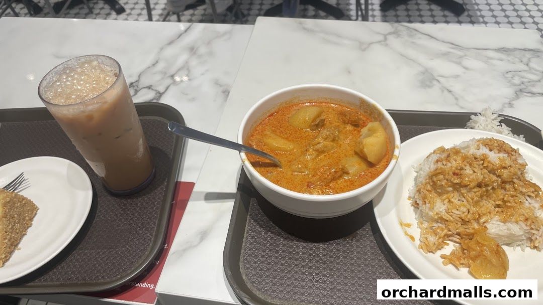 A tray with a glass of iced tea, a bowl of curry with rice, and a slice of cake.