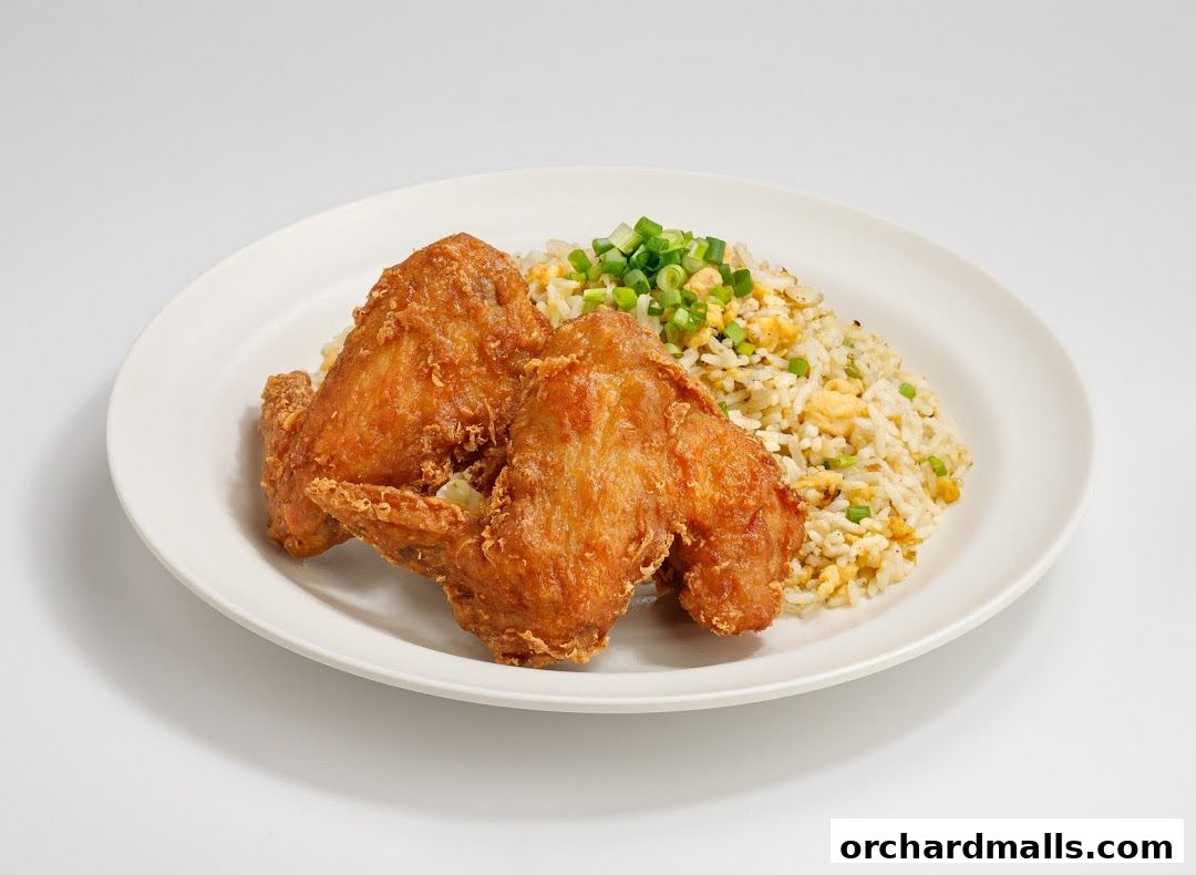 A plate of crispy fried chicken wings served with fried rice and chopped scallions.