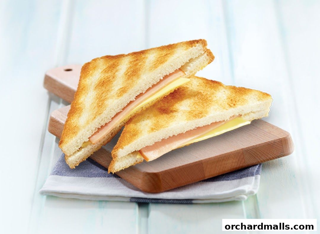 Two triangular ham and cheese sandwiches on wooden boards with a striped napkin.