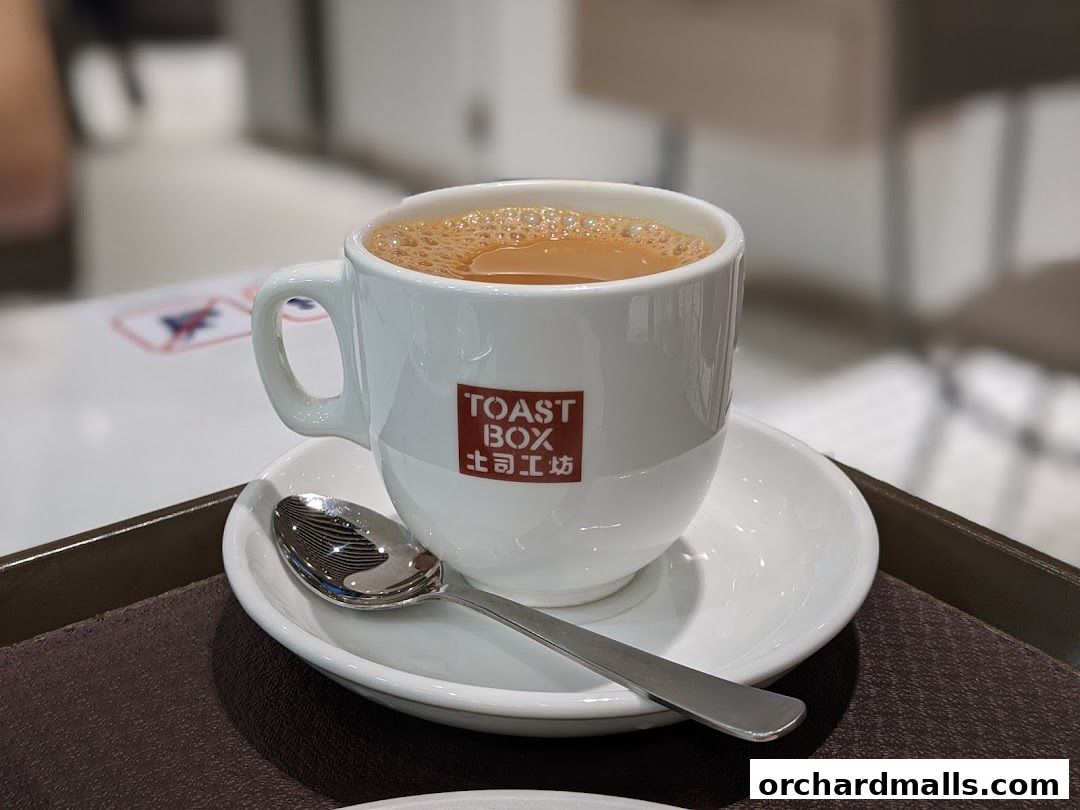 A cup of coffee with the Toast Box logo and a spoon on a saucer.