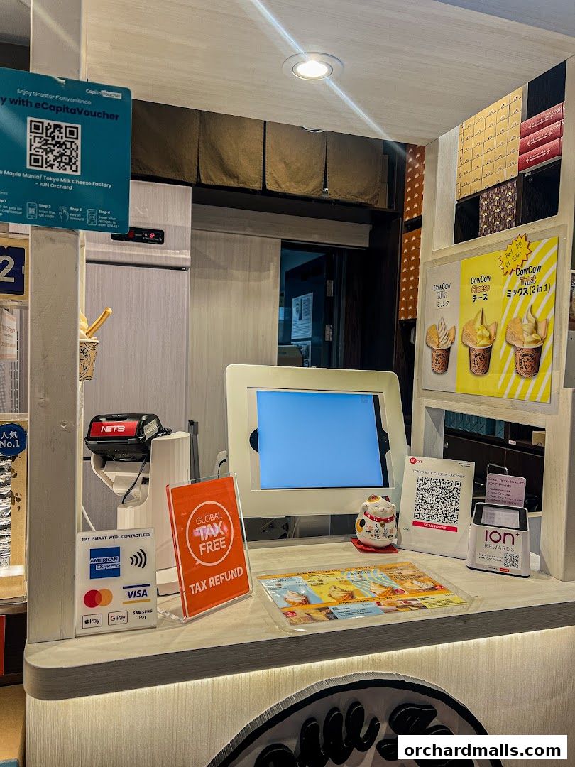 A counter at Tokyo Milk Cheese Factory with payment terminals, promotional signs, and product displays.