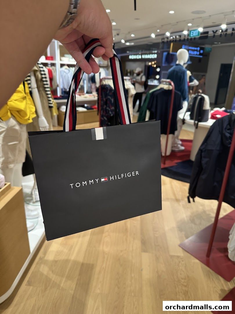A person holds a Tommy Hilfiger shopping bag inside a brightly lit store.