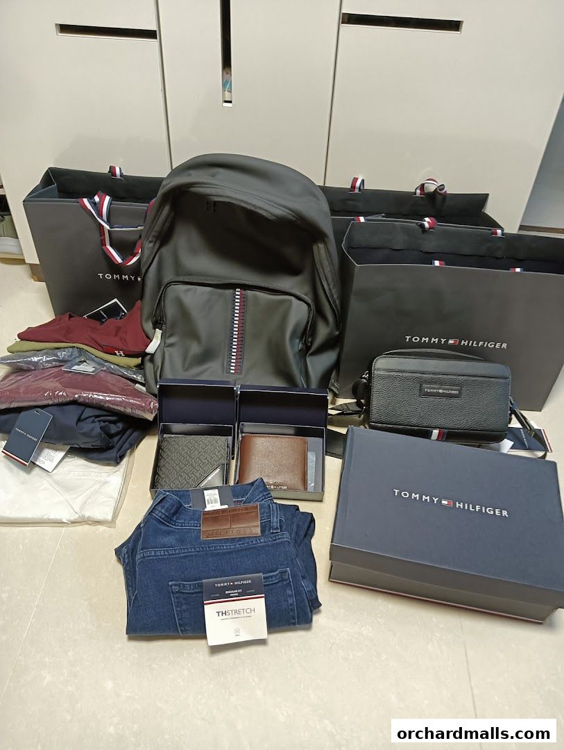 A collection of Tommy Hilfiger merchandise including a backpack, wallets, jeans, and shopping bags.