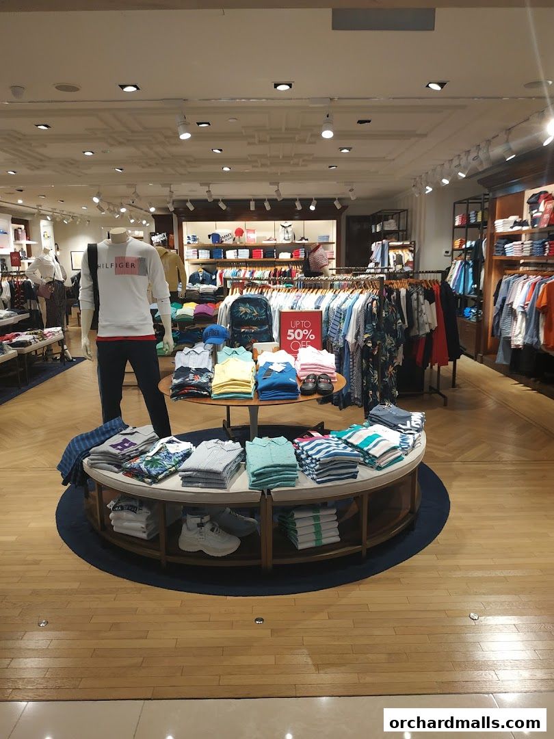 Interior of a Tommy Hilfiger store showcasing folded shirts, mannequins, and racks of clothing.