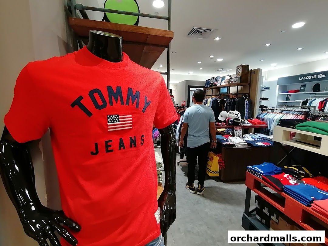 Mannequin in red Tommy Jeans shirt inside a well-lit clothing store.