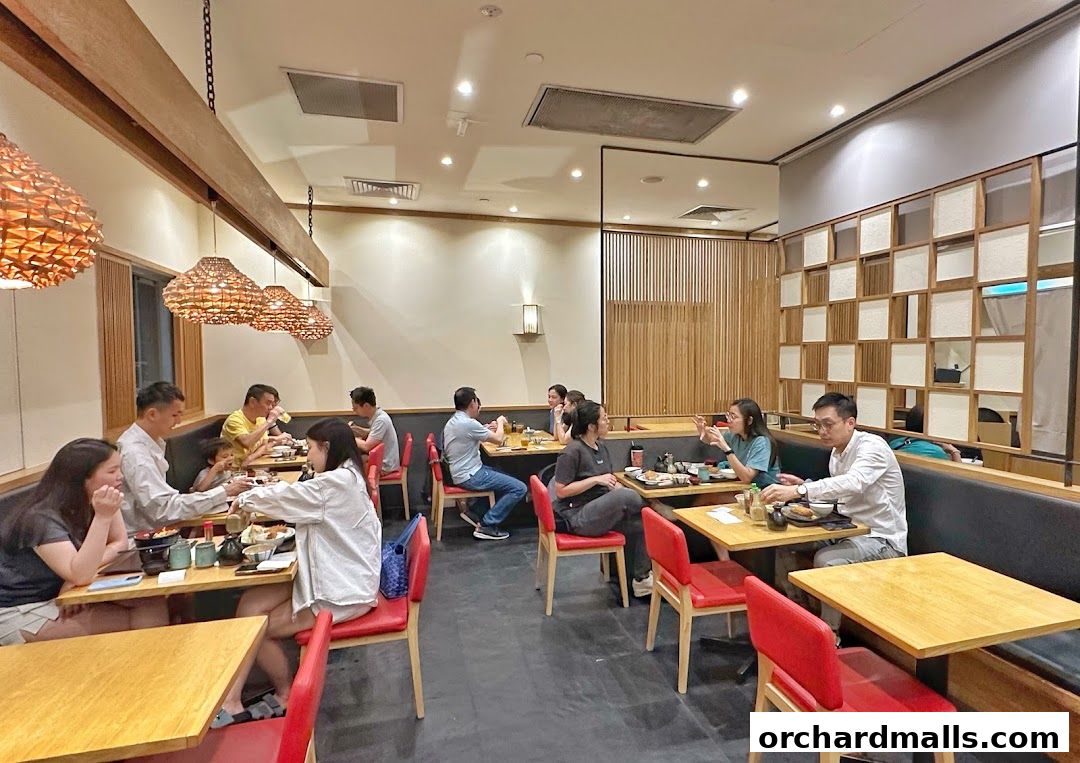 Diners enjoy meals at tables inside a modern Japanese restaurant with warm lighting and wooden accents.