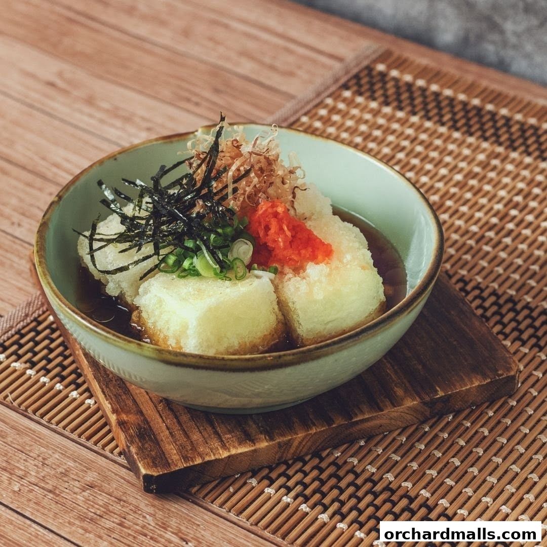 A bowl of Japanese Agedashi Tofu with garnishes on a wooden placemat.