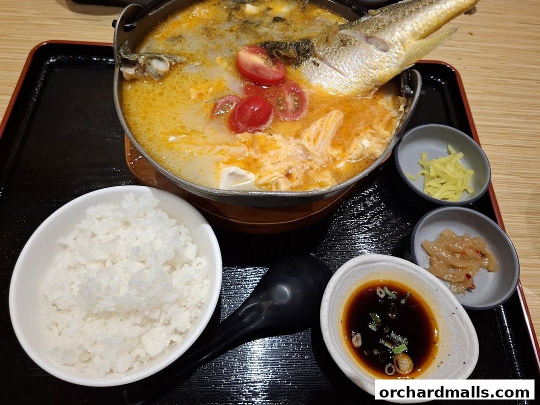 A hot pot dish with a whole fish, tomatoes, and rice, served with side dishes.