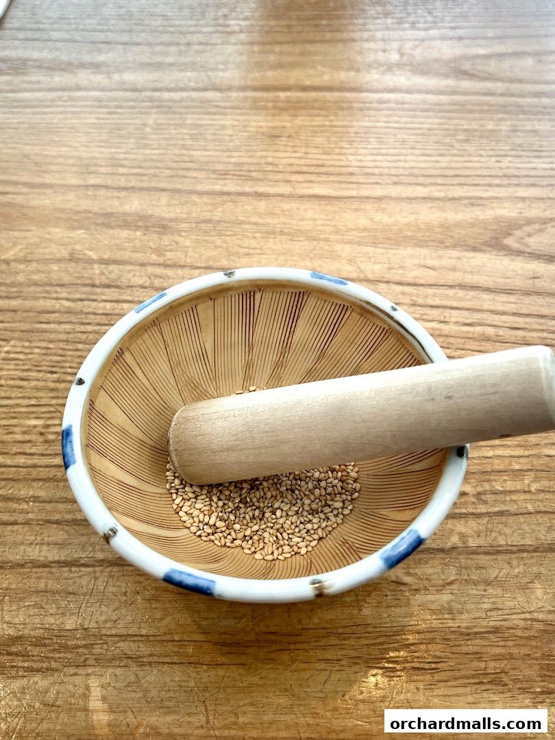A mortar and pestle with sesame seeds on a wooden table.