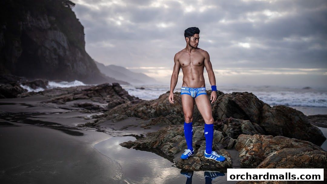 A man models athletic underwear and socks on a rocky beach.