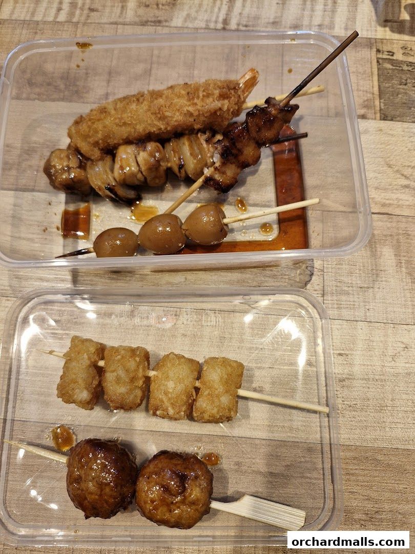 Two clear containers filled with various grilled skewers and fried items.