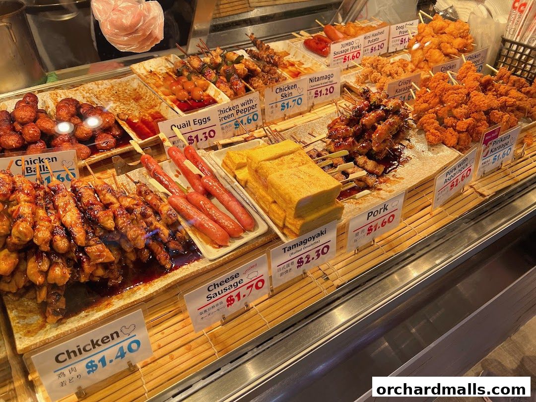 A display of various Japanese skewers and fried items with price labels.