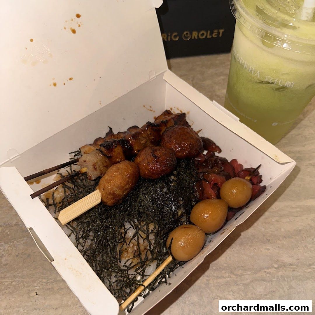 A bento box filled with grilled skewers, rice, and pickled items, next to a green drink.