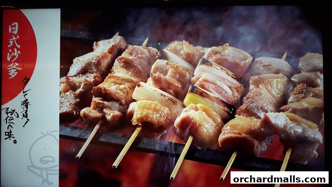 Close-up of delicious yakitori skewers grilling over flames, with Japanese text on the side.