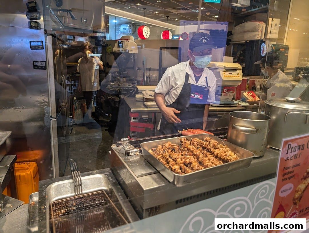 Chefs preparing skewers and food behind a glass counter at TORI-Q.