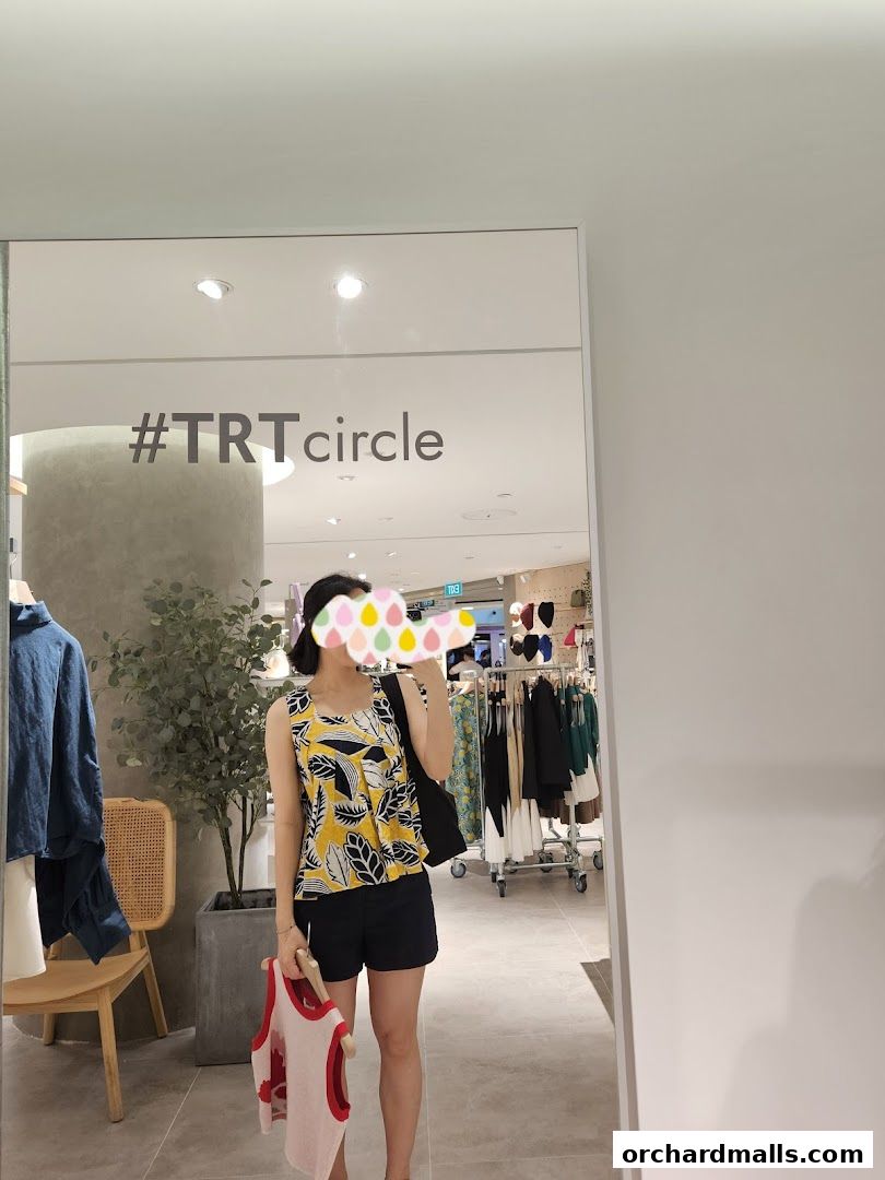 A woman stands in front of a mirror in a clothing store, holding a garment.