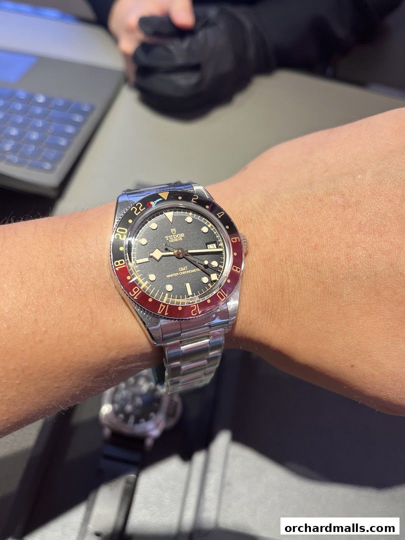 A close-up of a Tudor GMT watch on a wrist, with a salesperson in the background.