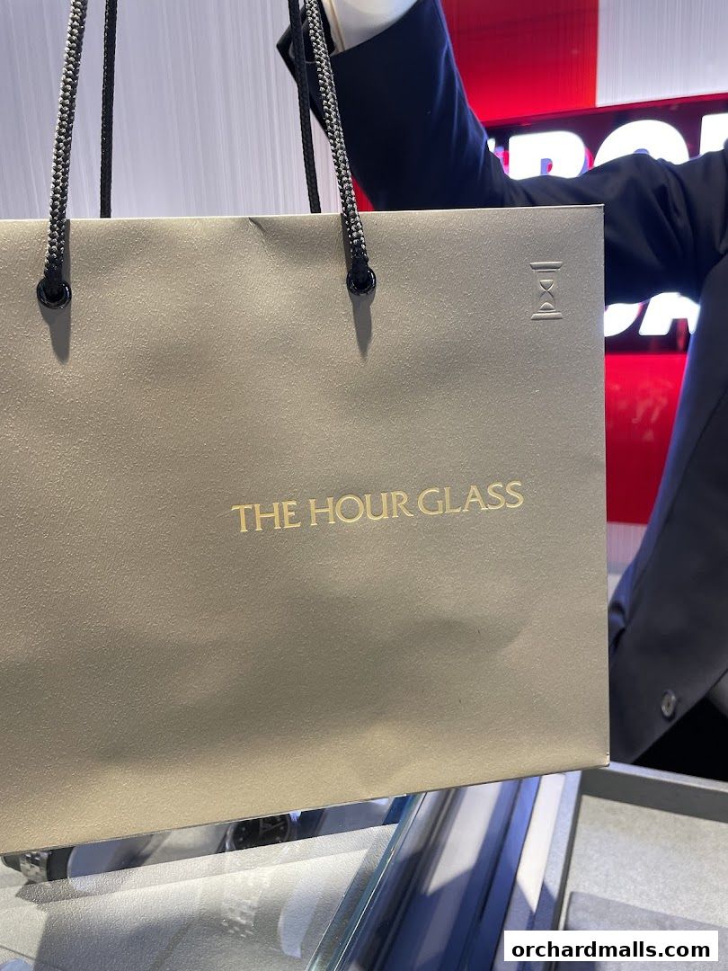 A person holds a shopping bag from The Hour Glass, a luxury watch retailer.