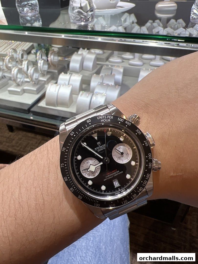 A close-up of a person wearing a Tudor chronograph watch in front of a display case.