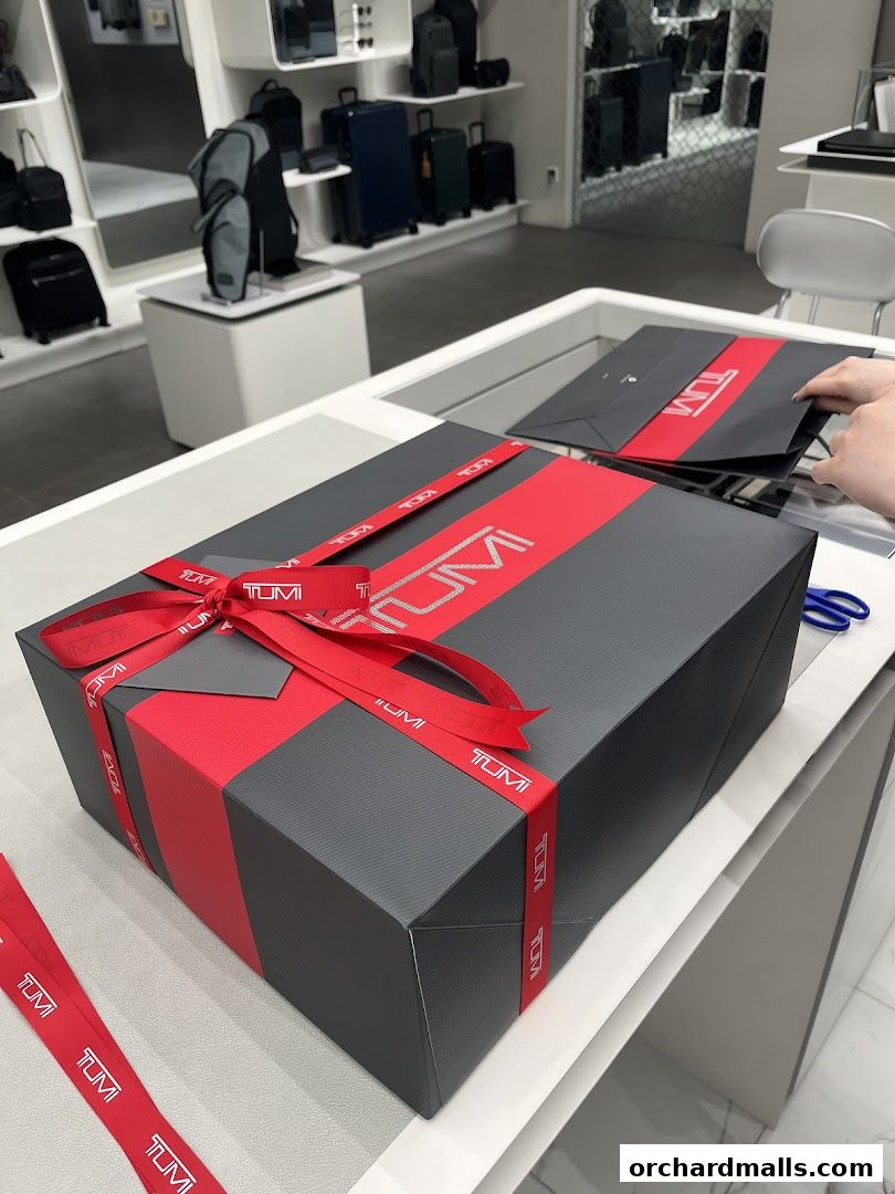 A beautifully wrapped TUMI gift box with red ribbon and branding, inside a store.