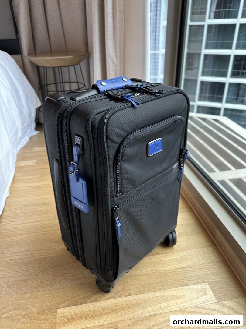 A black TUMI suitcase with blue accents sits on a wooden floor near a window.