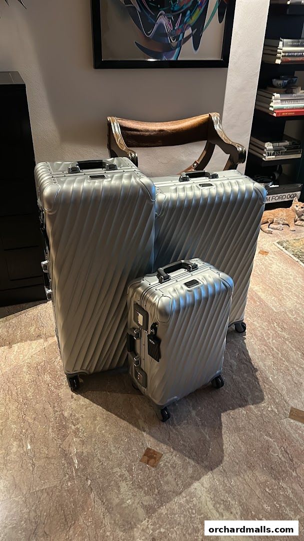 Three sleek silver TUMI suitcases of varying sizes are displayed on a marble floor.