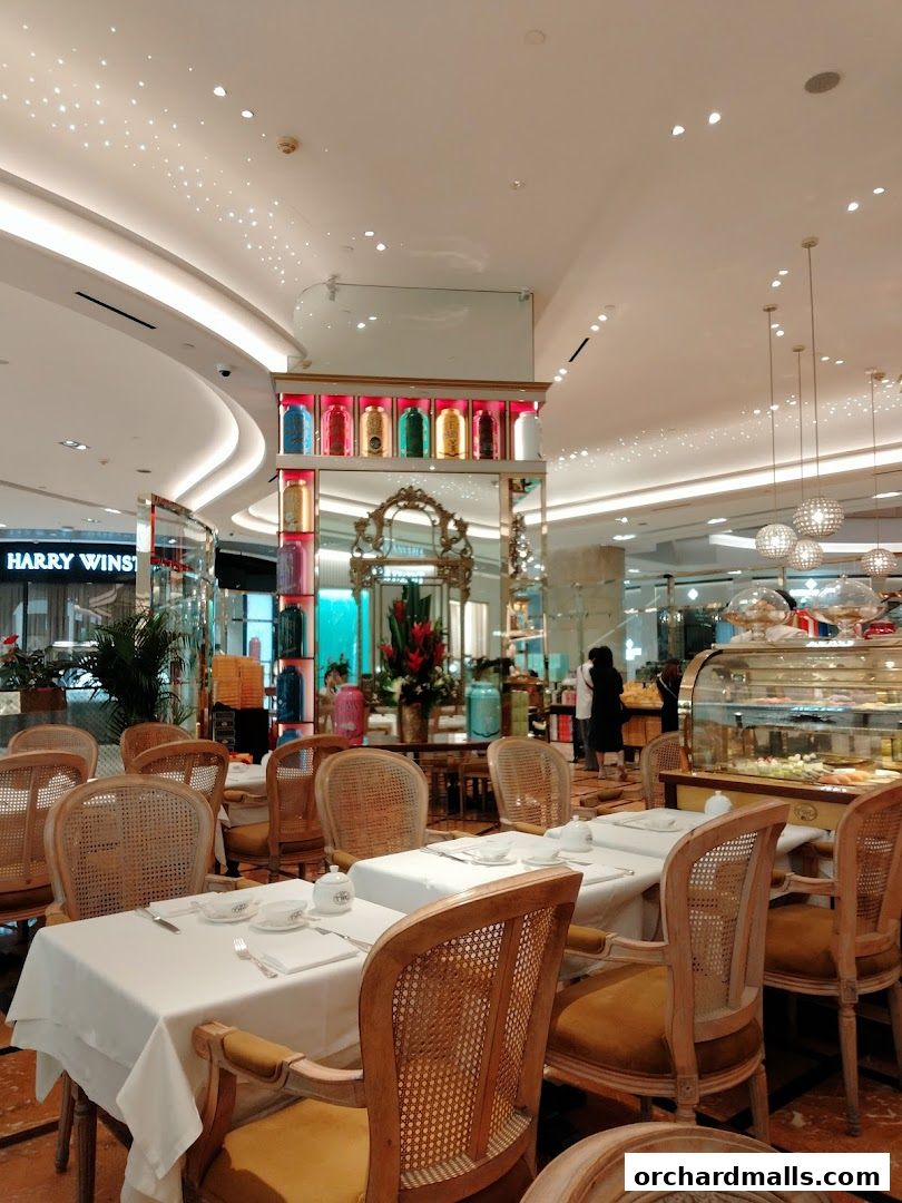 Elegant dining area with white-clothed tables and ornate chairs, featuring a display of tea canisters.