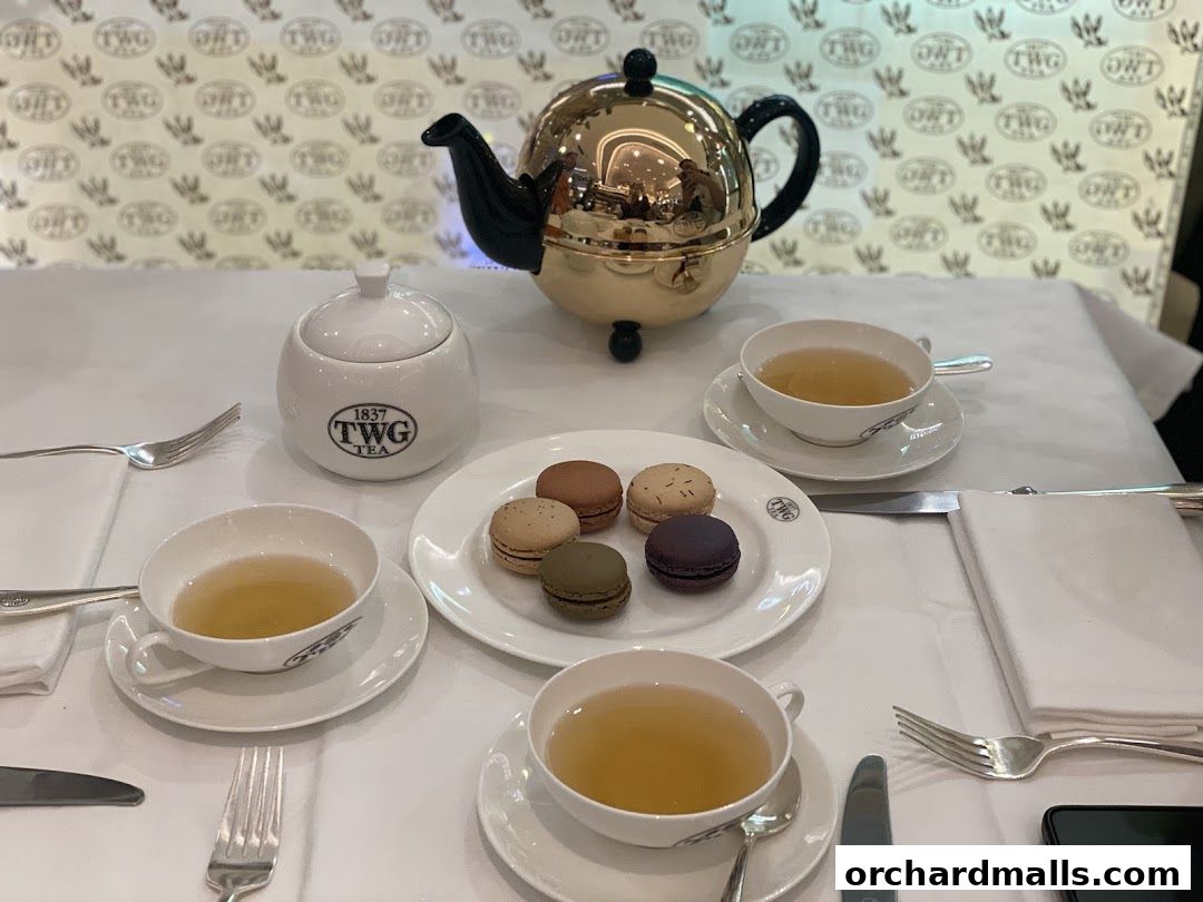 A table setting at TWG Tea with macarons, tea cups, and a golden teapot.