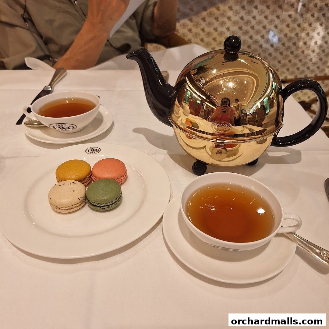A table setting with a golden teapot, cups of tea, and macarons at TWG Tea.