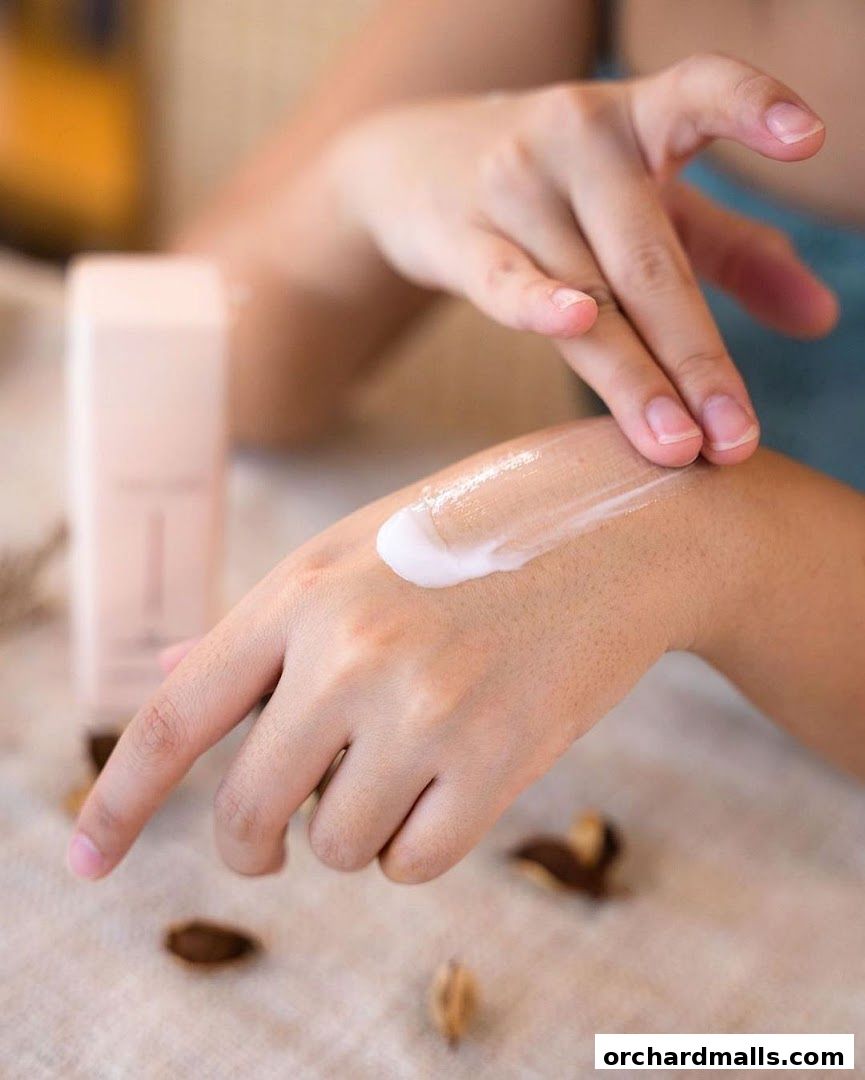A person applies a creamy lotion to their hand, with a product bottle in the background.