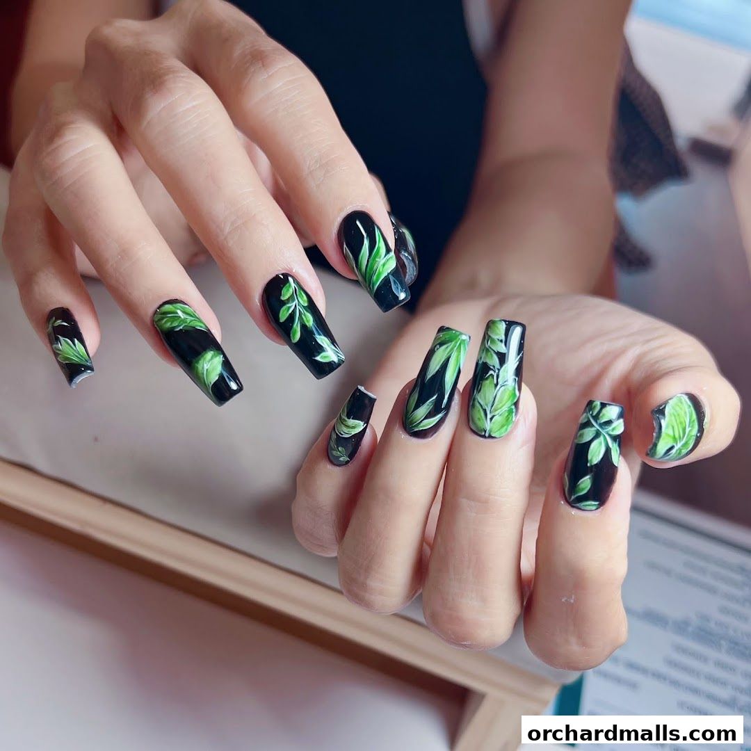 Close-up of hands with black nails adorned with green leaf designs.