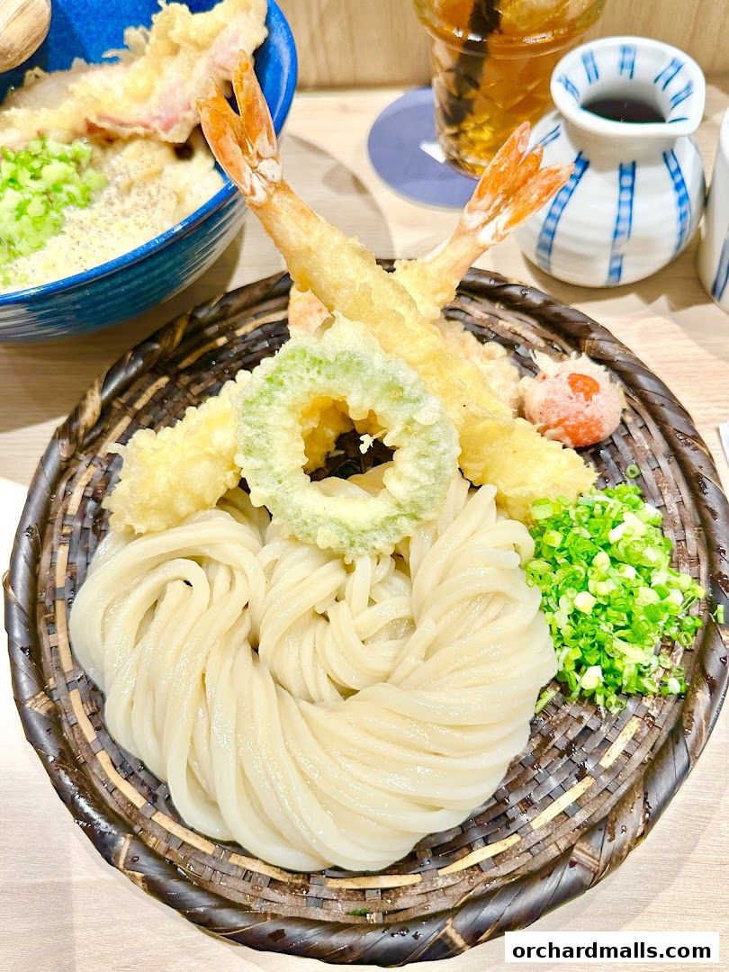 A close-up of a delicious udon noodle dish with tempura shrimp and vegetables.