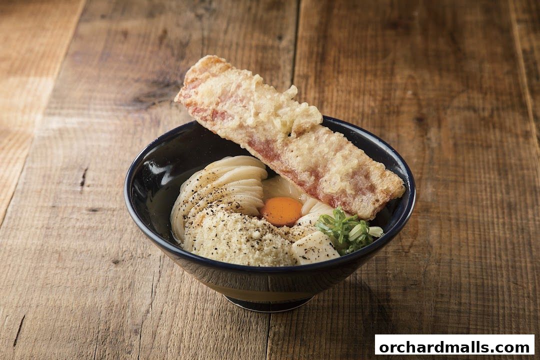 A bowl of udon noodles with tempura and a raw egg yolk on a wooden table.