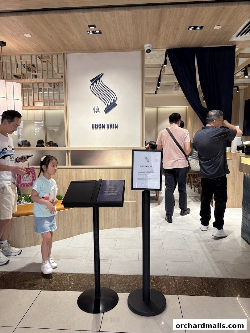 People queuing at Udon Shin Singapore, with the restaurant logo visible.