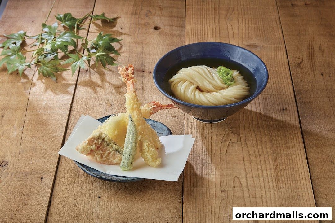A bowl of udon noodles and a plate of tempura on a wooden table.