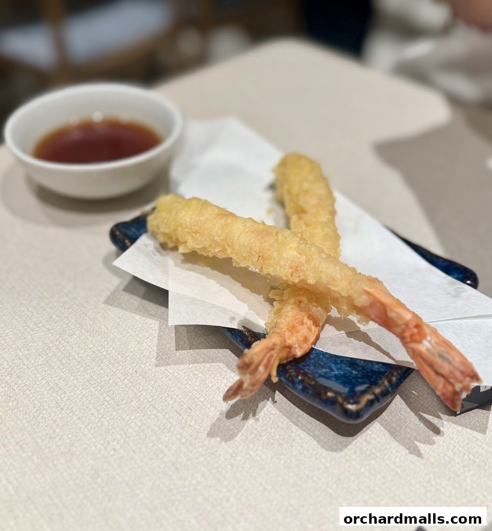 Crispy tempura prawns served with a dipping sauce on a dark blue plate.