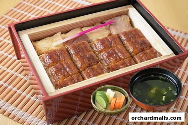 A close-up of a delicious Unagi bento box with grilled eel, rice, pickles, and soup.