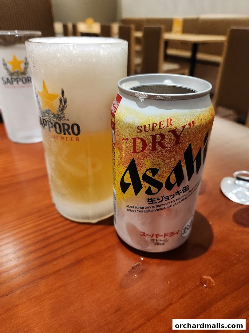 A glass of Sapporo beer and an open can of Asahi Super Dry on a wooden table.