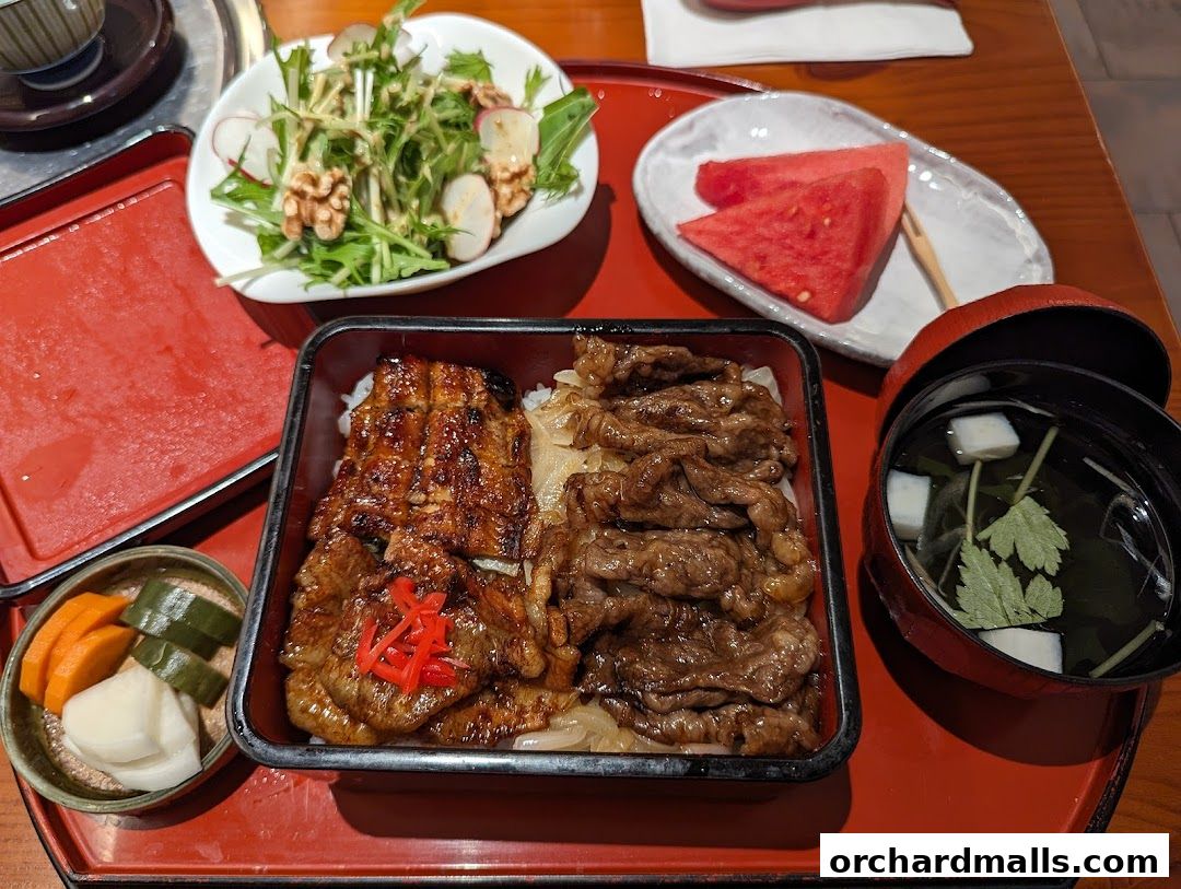 A bento box with grilled eel and beef, served with salad, pickles, watermelon, and soup.