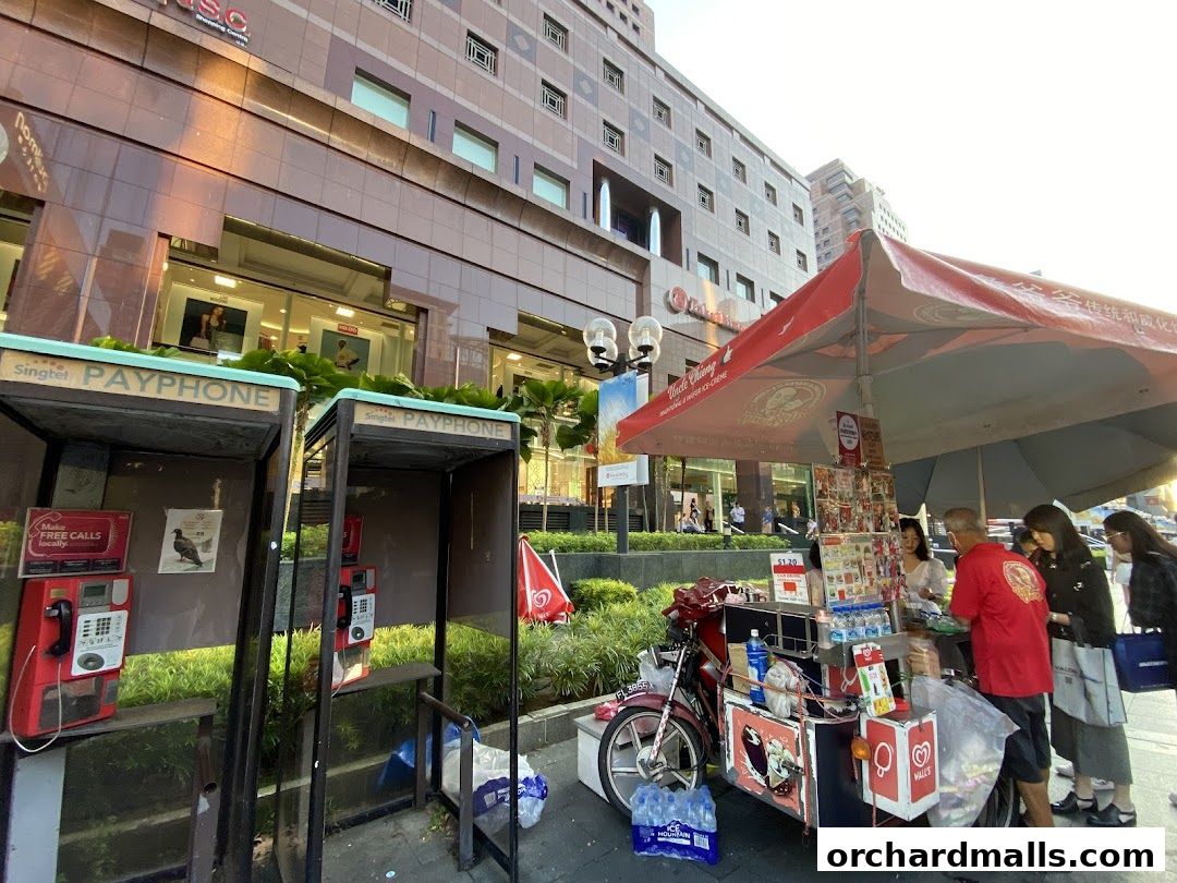 An ice cream cart with people buying ice cream in front of a building.