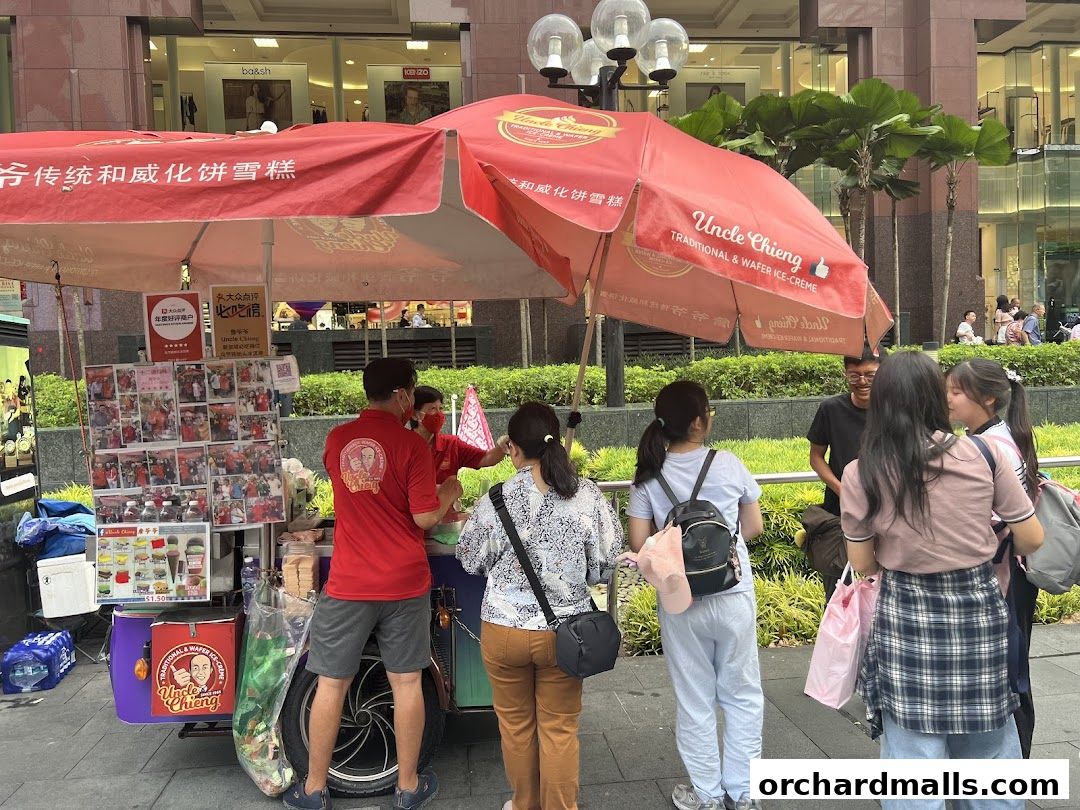 A street vendor sells traditional wafer ice cream under a red umbrella, with customers waiting.