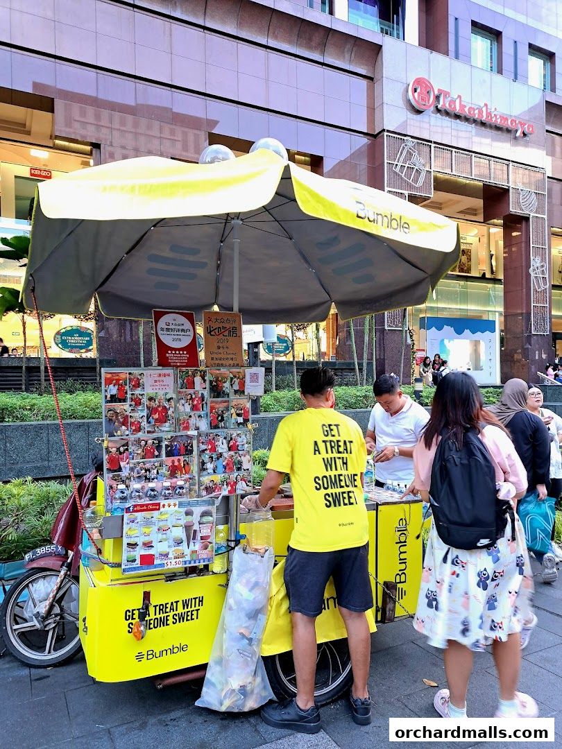 A bright yellow ice cream cart with a yellow umbrella, serving customers on a city street.