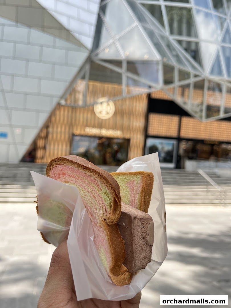 A hand holds a traditional wafer ice cream sandwich with colorful bread and chocolate ice cream.