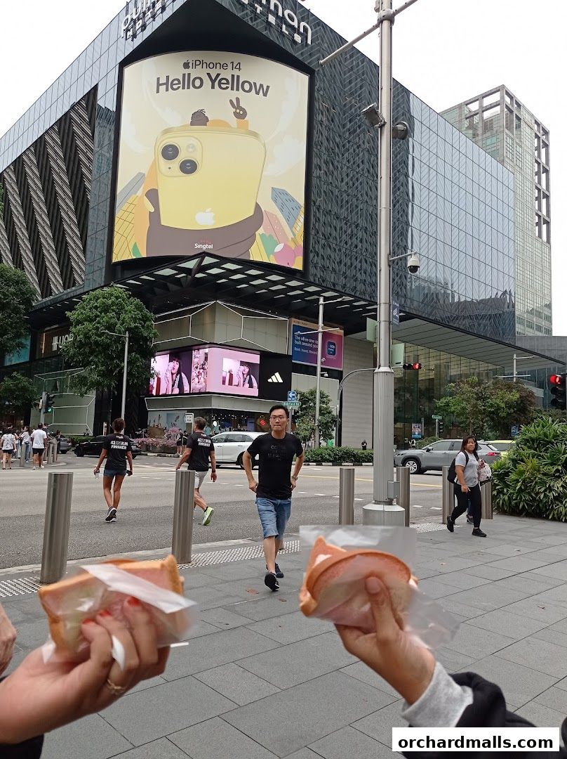 People walking on a street with a large digital billboard advertising an iPhone.