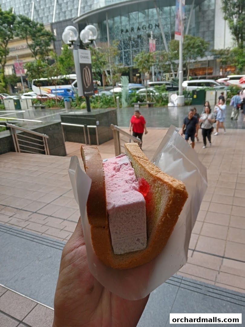A hand holds a traditional wafer ice cream sandwich with pink ice cream and jelly.