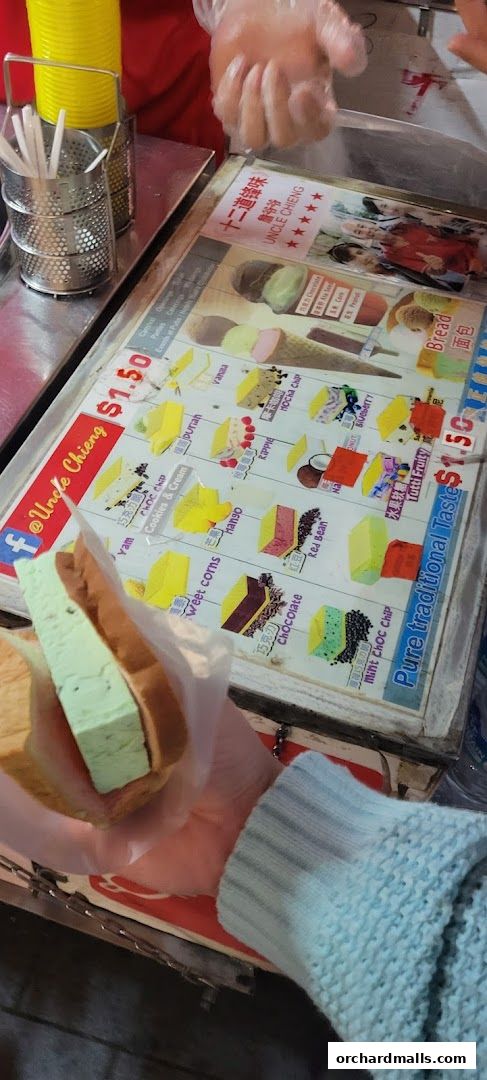 A person holds a traditional wafer ice cream sandwich with a menu board in the background.