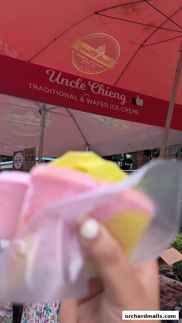 A hand holds colorful wafer ice cream cones under a red umbrella.