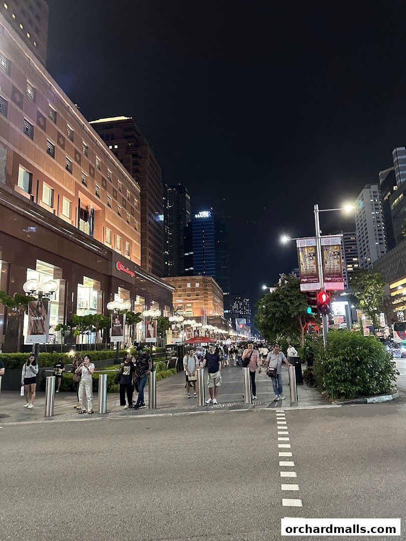 A bustling street scene at night with people walking past illuminated shops and tall buildings.