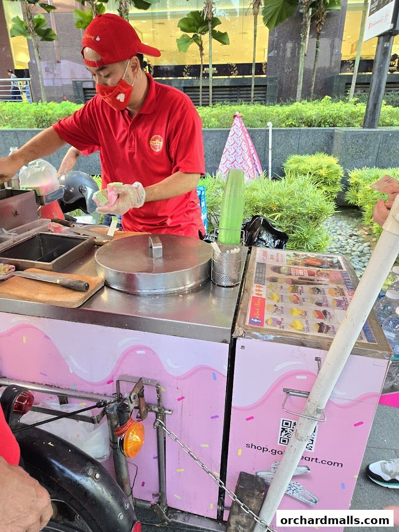A vendor prepares traditional wafer ice cream at a colorful pink cart.