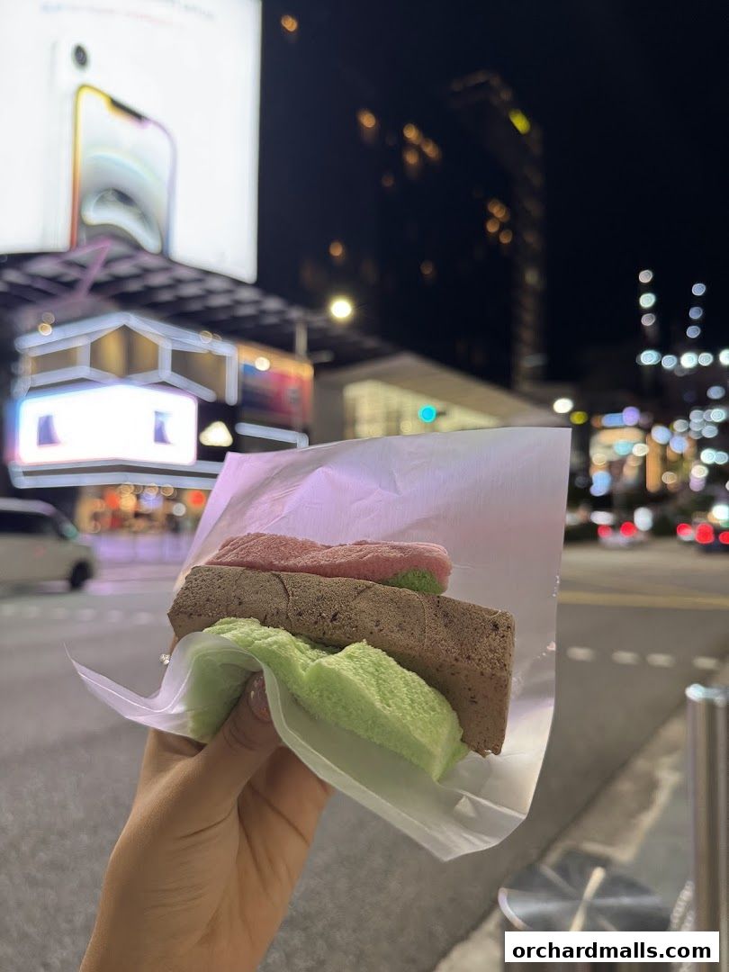 A hand holds a traditional wafer ice cream with three colorful layers.